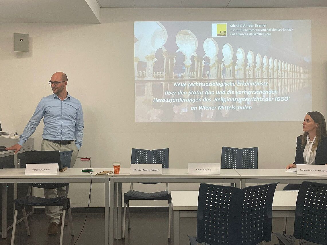 Image: Photo of the lecturer Michael Kramer, in the background a PowerPoint slide; prae doc Tamara Nili-Freudenschuß is sitting at the right edge of the picture