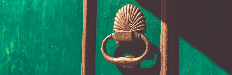 A golden door knocker on a green door