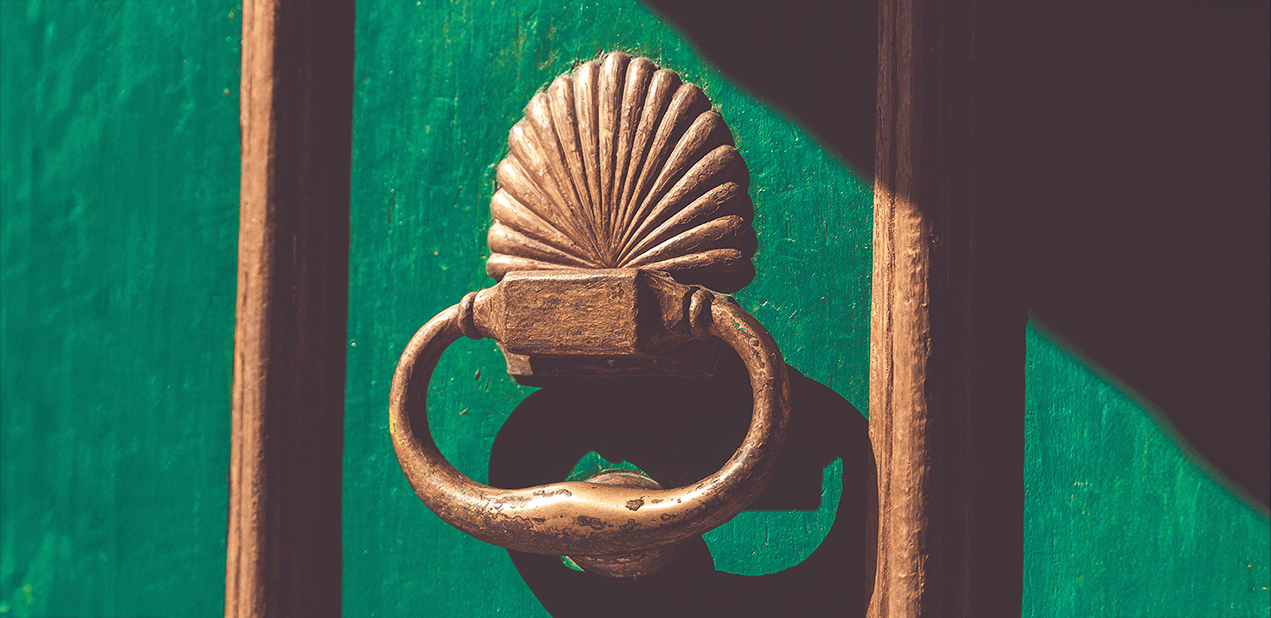 A golden door knocker on a green door